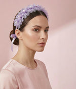Woman wearing a lilac floral hair accessory with a plain background 