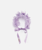 Woman wearing a lilac floral hair accessory with a plain background 