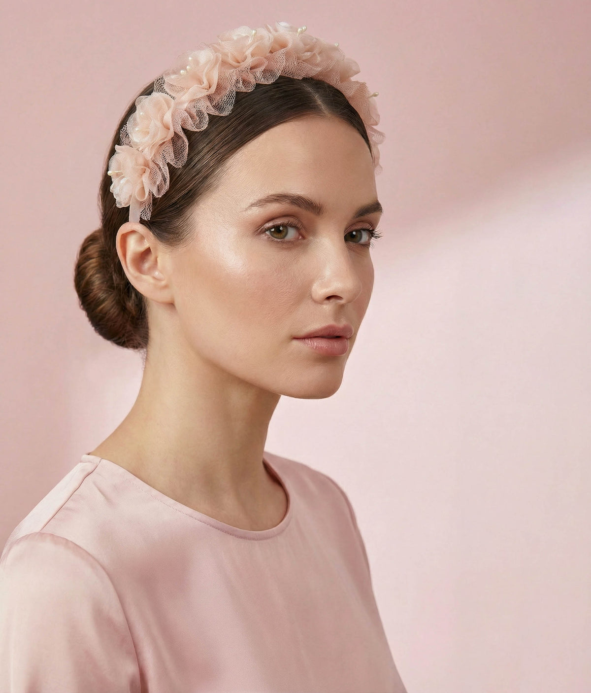 Woman wearing a pink floral hair accessory with a plain background 
