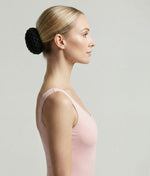 Woman wearing a pink top with a decorative hair accessory on a plain background 