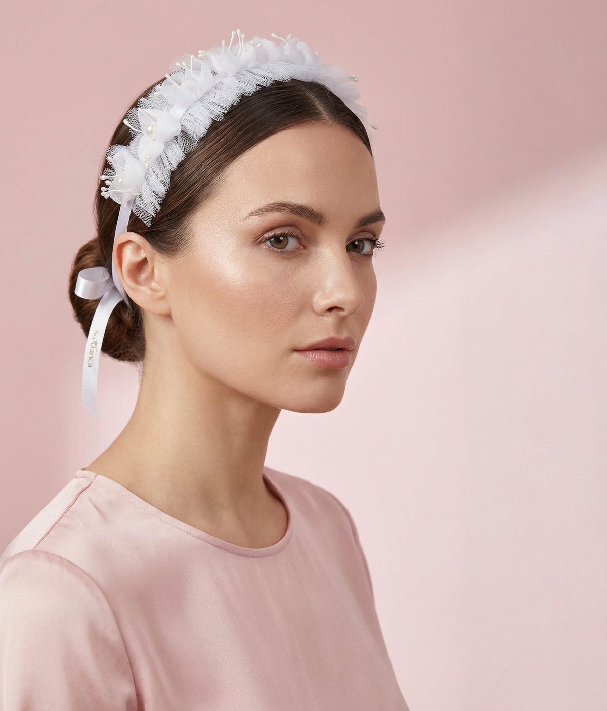 Woman wearing a white floral hair accessory with a plain background 