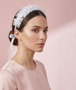 Woman wearing a white floral hair accessory with a plain background 