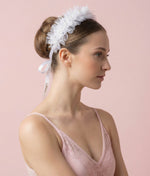 Woman wearing a white floral hair accessory with a plain background 