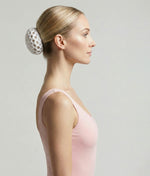 Woman wearing a pink top with a decorative hair accessory on a plain background 