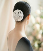 Woman wearing a pink top with a decorative hair accessory on a plain background 