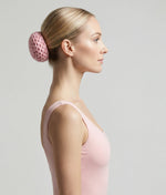 Woman wearing a pink top with a decorative hair accessory on a plain background 